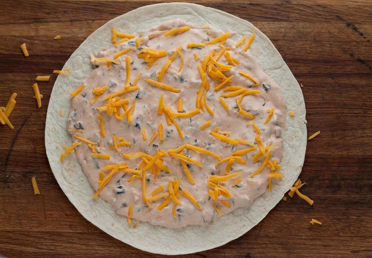 A tortilla topped with cream cheese mixture and shredded cheese.