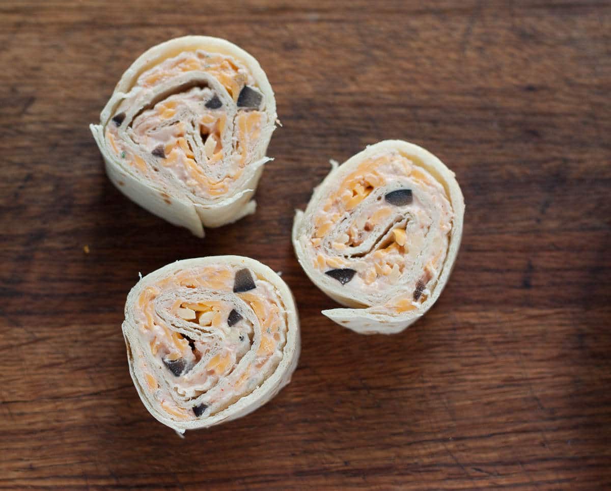 Three Fiesta Ranch Cream Cheese Pinwheels on a wooden surface.