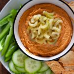 A bowl of buffalo ranch hummus with vegetables on a platter.