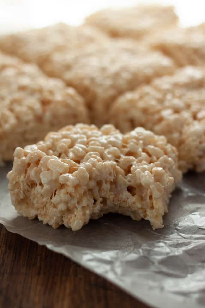 Coconut Rice Krispie treats cut into squares with a bite missing from the one in front.