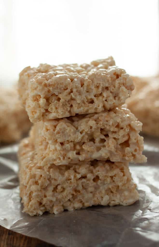 A stack of coconut marshmallow treats on a piece of wax paper with more in the background.