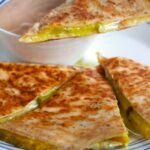 A dill pickle quesadilla on a plate cut into wedges.