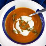 A bowl of roasted sweet potato soup topped with crema and pepitas.