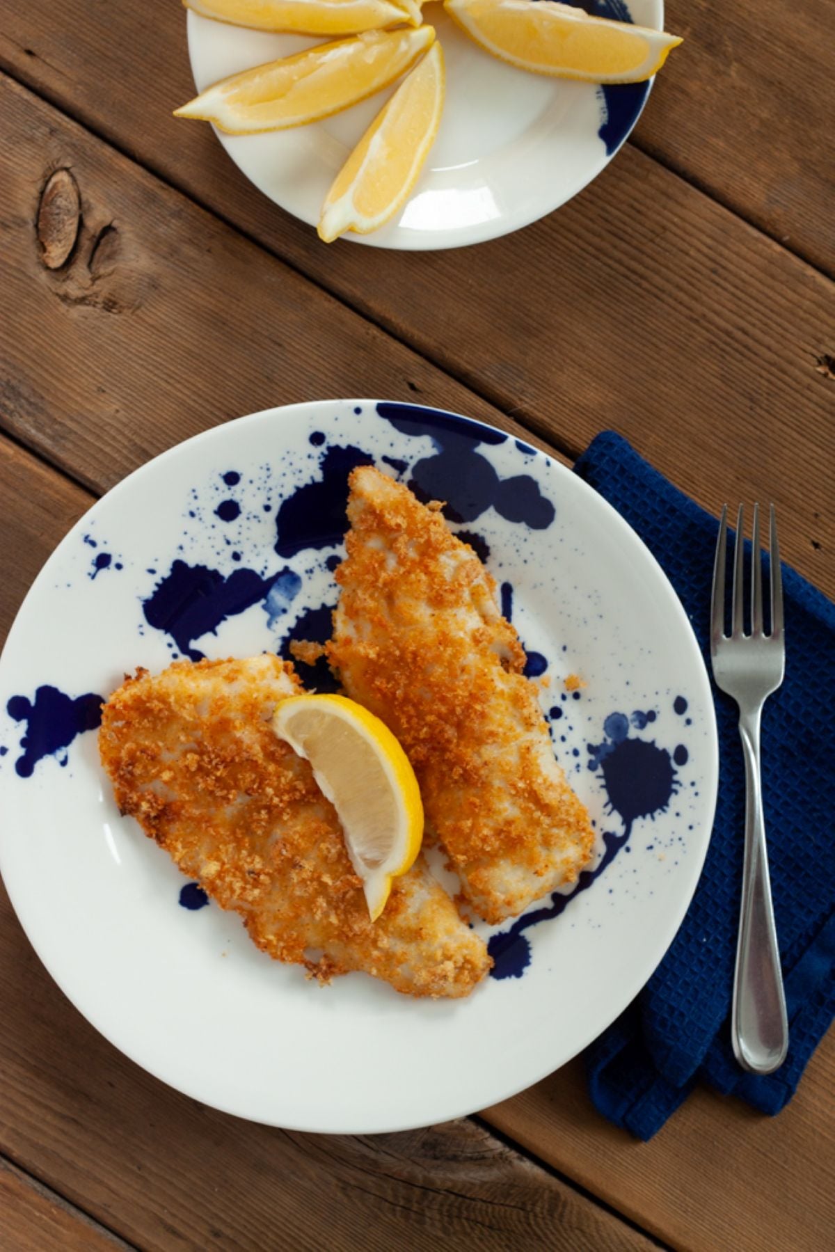 Two air fried walleye fish fillets on a plate with a slice of lemon.