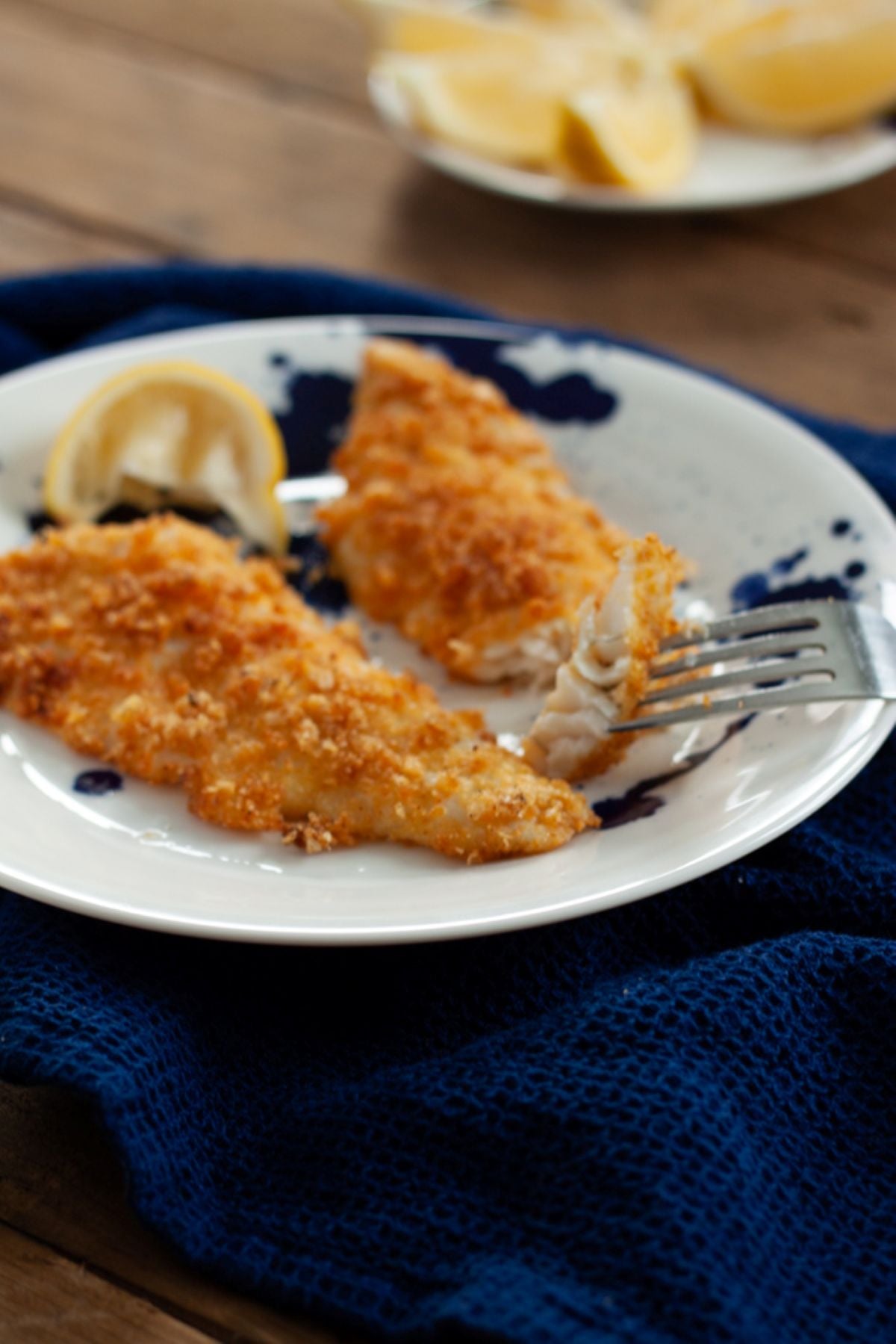 Two air fried walleye fish fillets on a plate with a slice of lemon. and a fork cutting into one of the fillets.