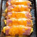 Salsa ham egg and cheese roll ups on a baking tray topped with melted cheese.