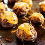 Chorizo stuffed mushrooms on a baking sheet topped with melted cheddar cheese.