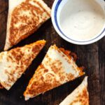 Vegetarian buffalo chickpea quesadilla cut into wedges next to a side of sauce.