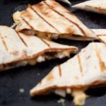 Grilled chicken quesadilla cut into wedges on a grill.