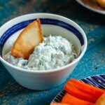 Spinach dip without mayonnaise in a bowl with a pita chip dipping in.