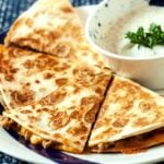 Ground turkey quesadilla cut into wedges on a plate with bowl of creamy sauce.