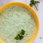 Creamy green sauce with spring onion in a yellow bowl on the table.
