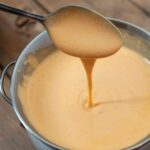 Chipotle blender hollandaise in a bowl with a spoon drizzling some back into it.