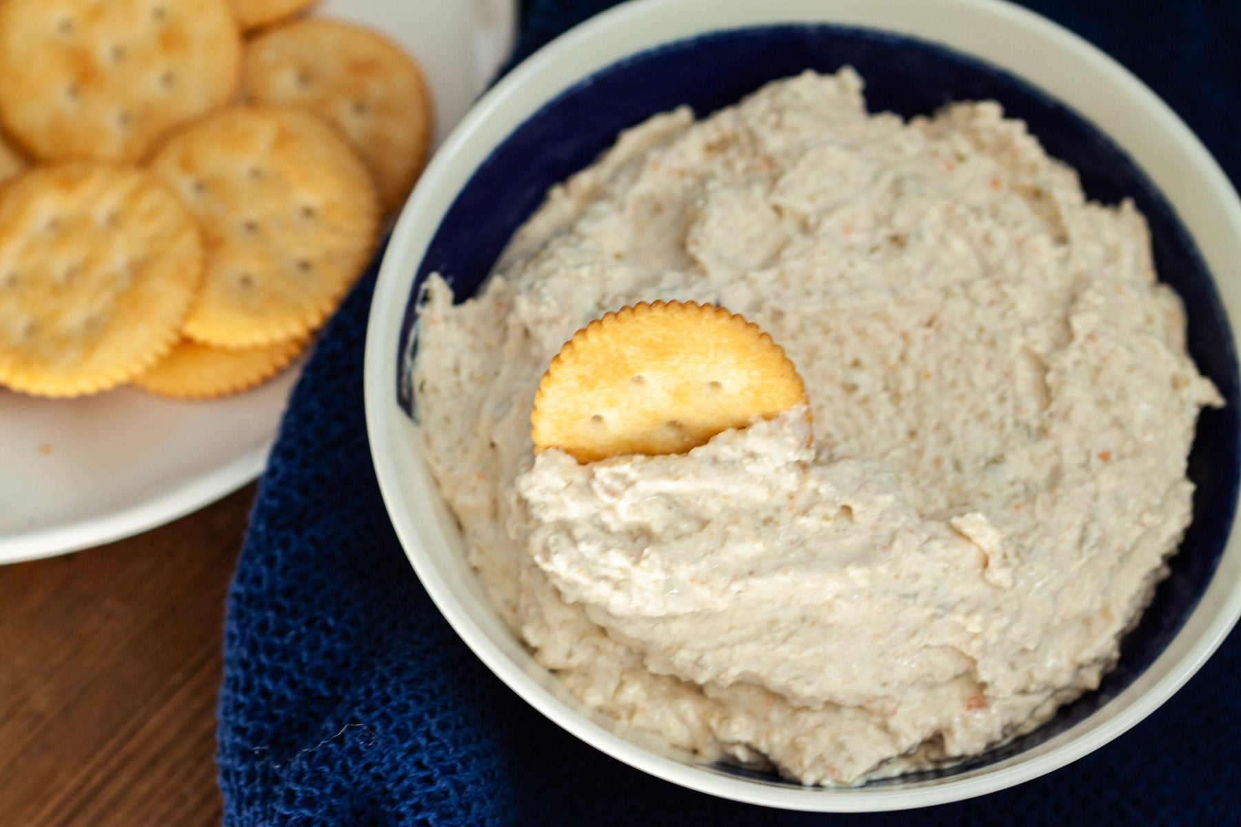 Green olive dip in a bowl next a plate of crackers.