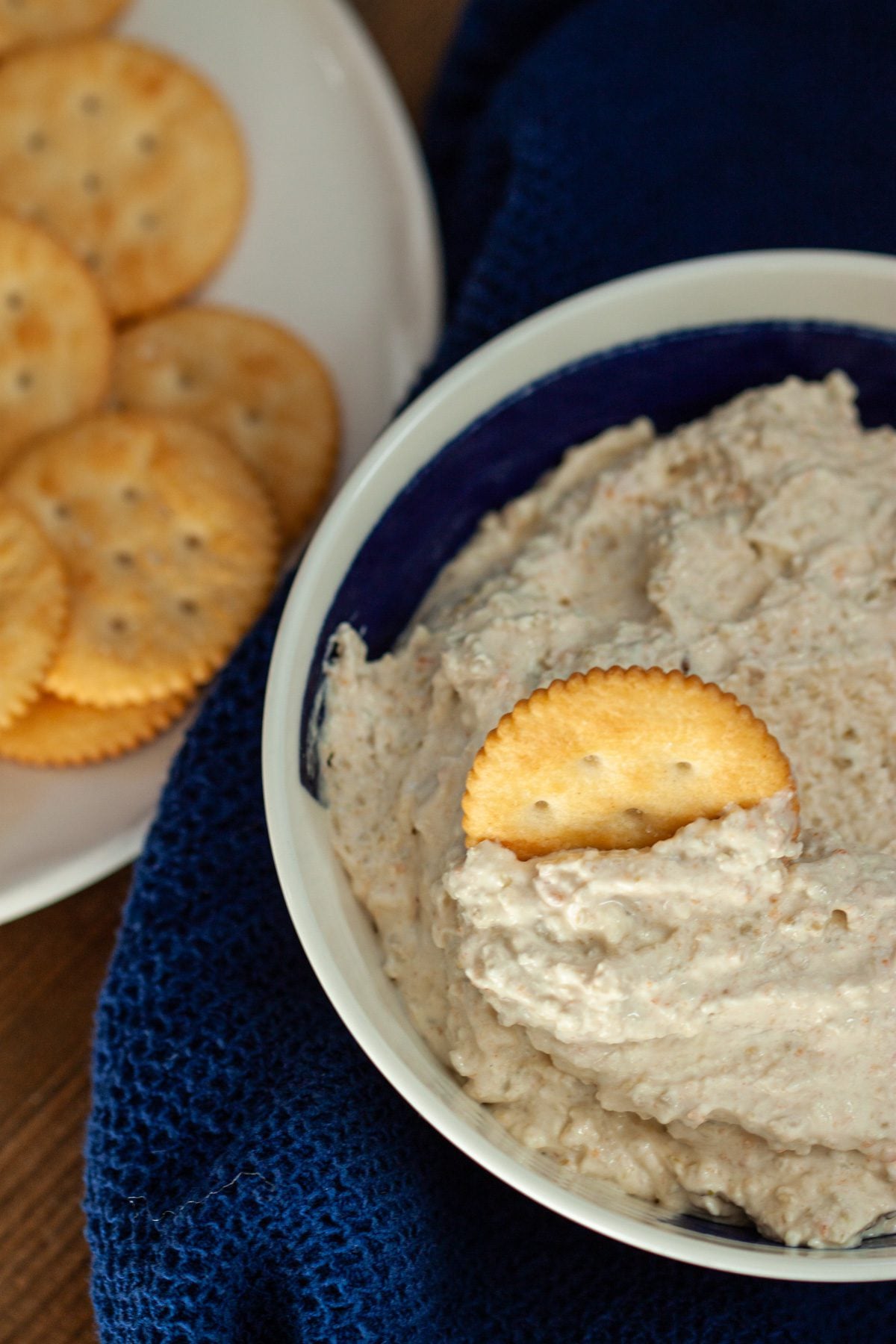 A bowl of green olive dip with a plate of crackers on the side.