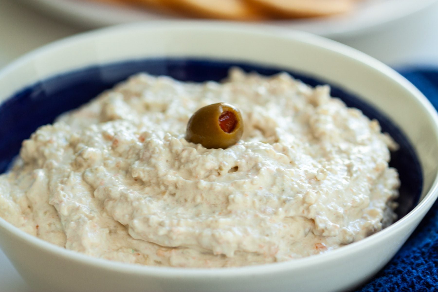 A bowl of olive dip with a green olive on top for a bit of garnish.