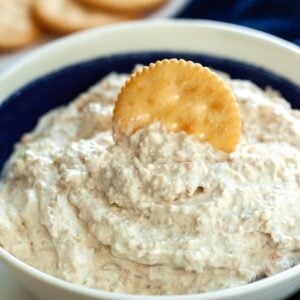A bowl of easy olive dip with a cracker dipping into it.