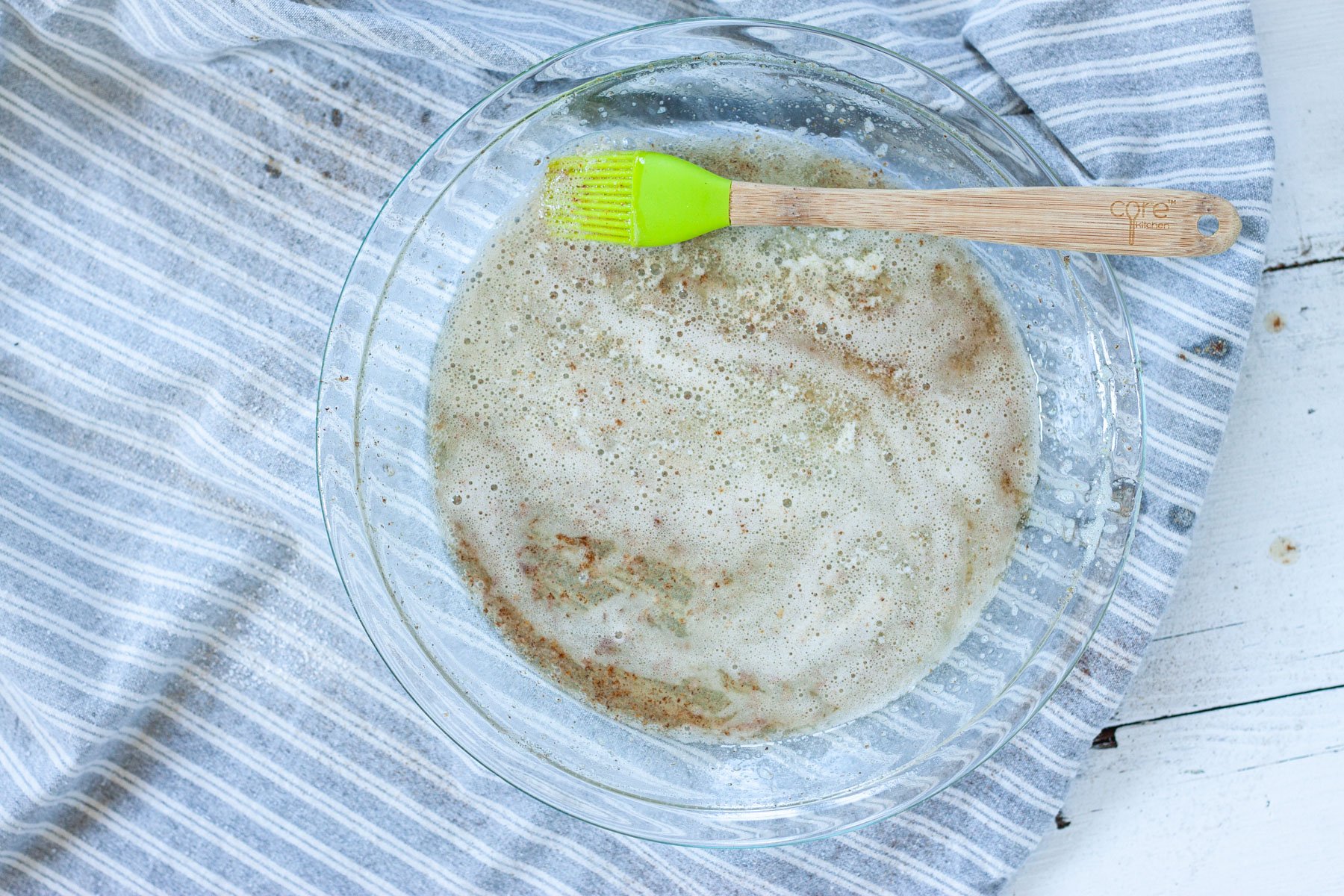 Melted butter in a pie plate with a silicone brush.