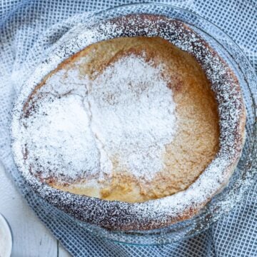 churro dutch baby in a pie pan garnished with powdered sugar and cinnamon sugar mixture.