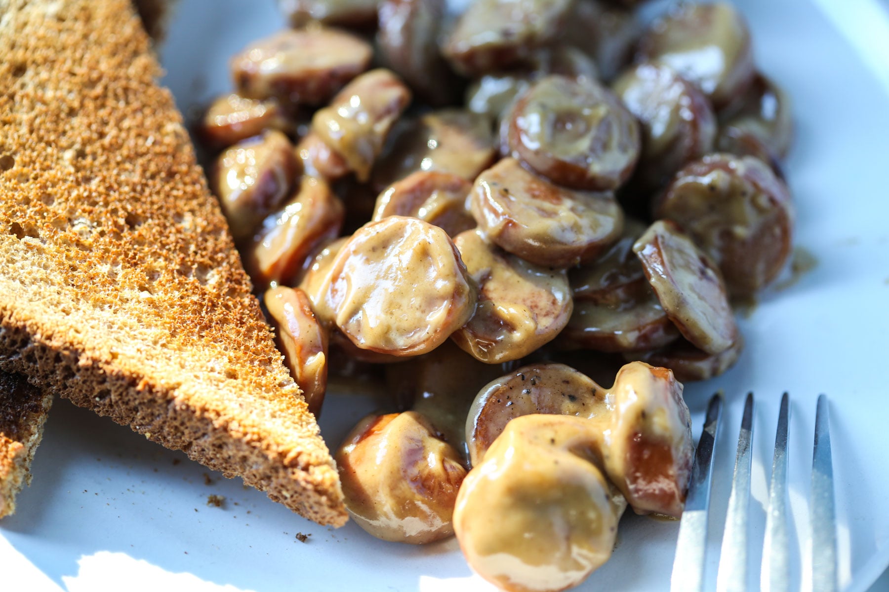 Dry toast with creamed sliced hot dogs on a white plate with a fork. 