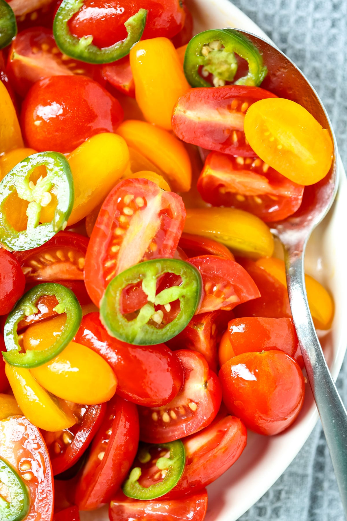 Spicy marinated tomato salad in a bowl with a large serving spoon.