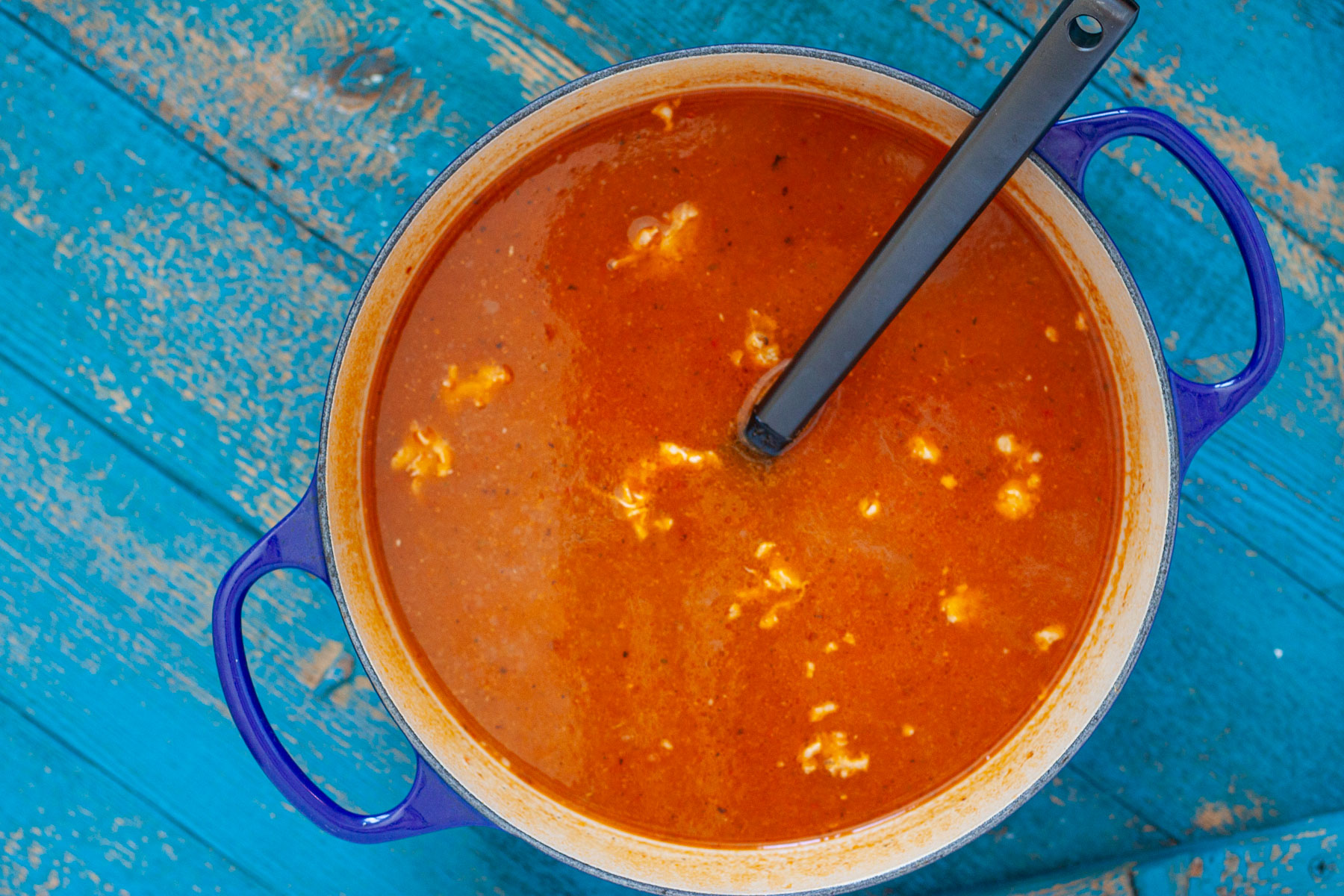 Chicken tortilla soup finished in a Dutch oven with a soup ladle.