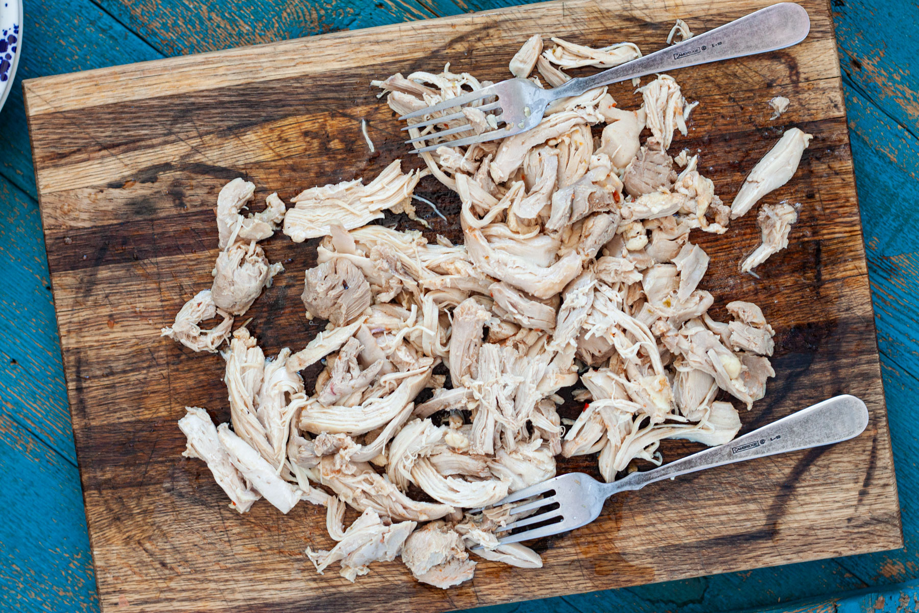 Chicken thighs shredded on a cutting board with two forks.