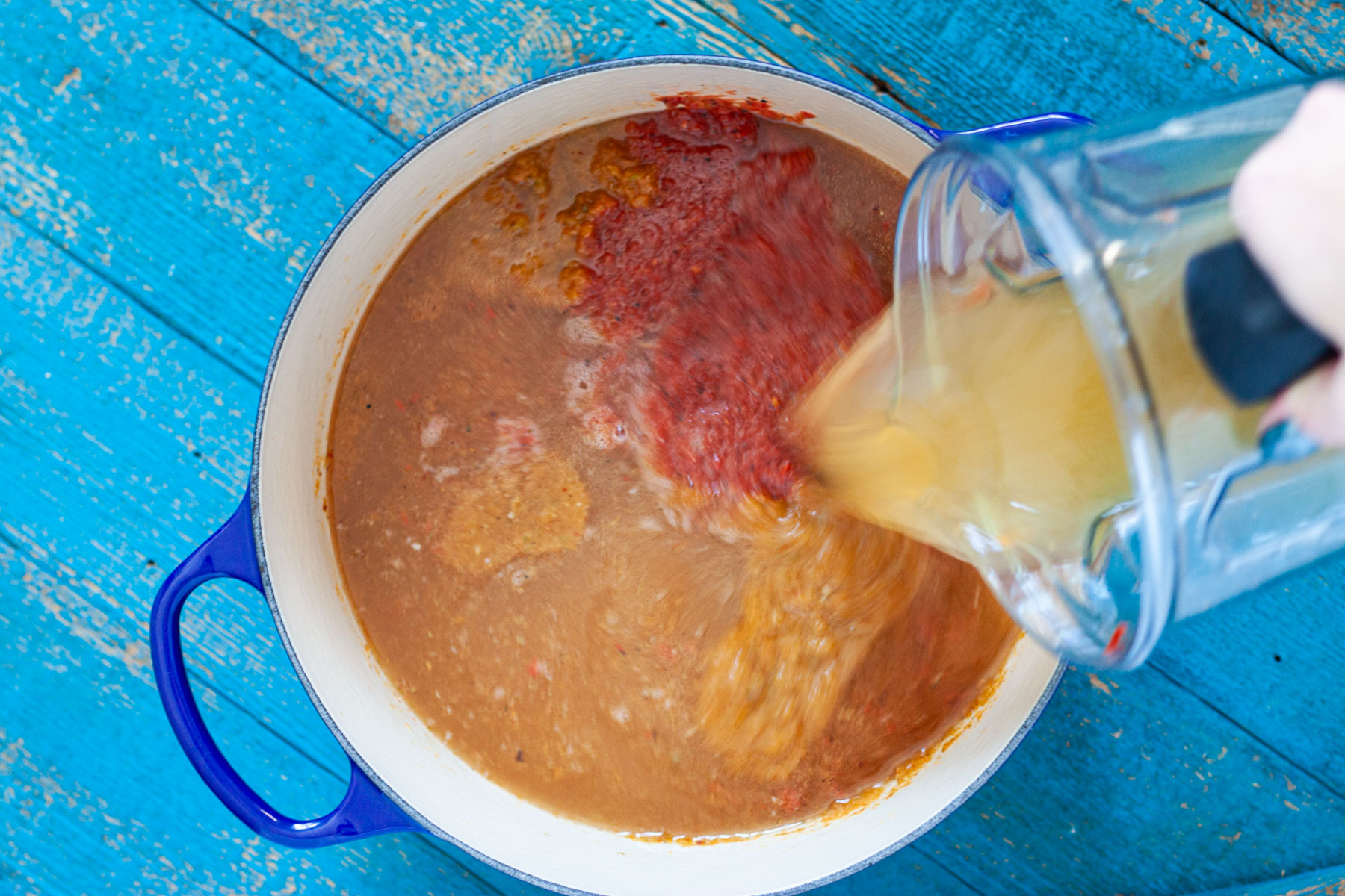 Adding chicken broth to the soup in a Dutch oven.