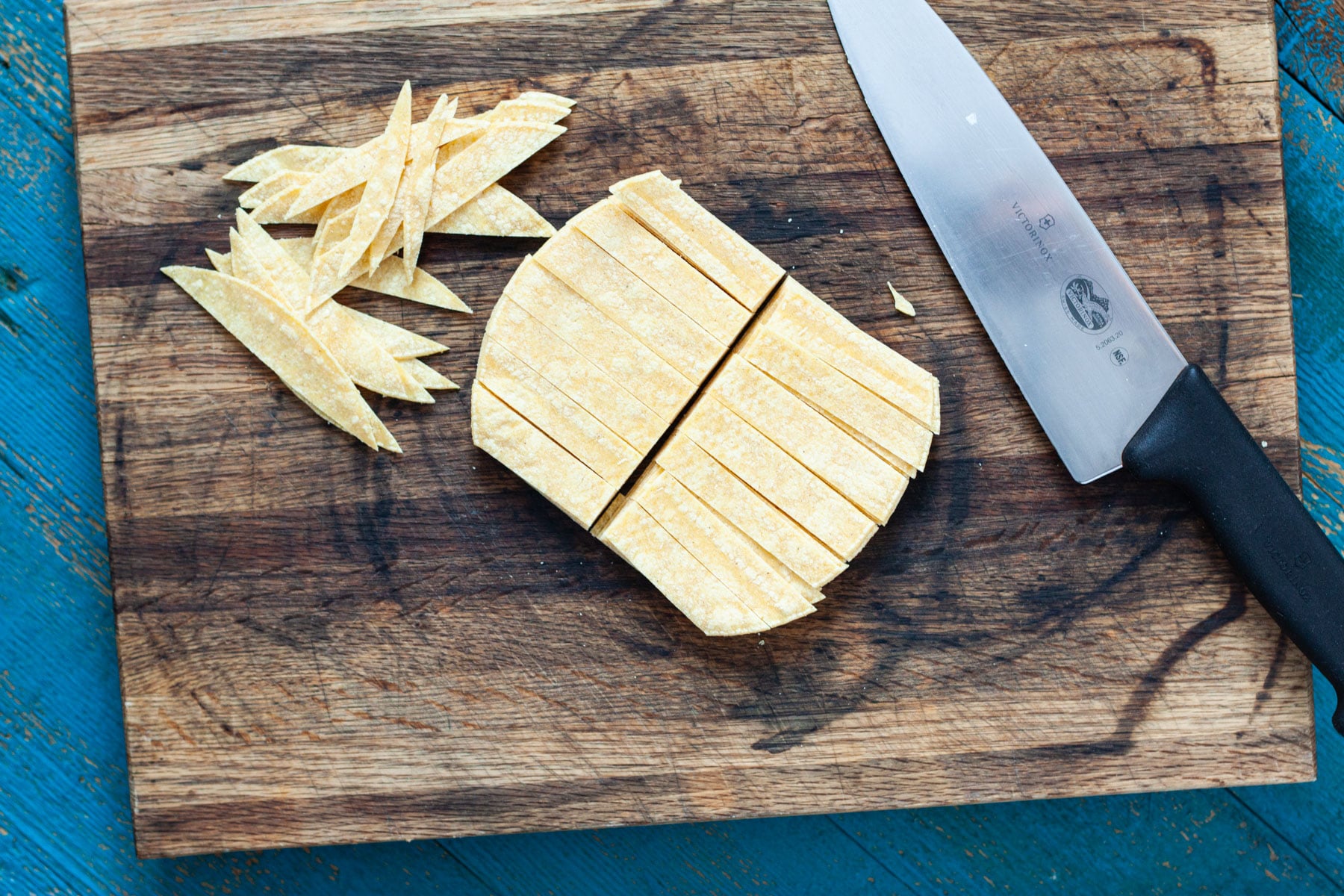 corn tortillas on a cutting board being cut into strips.