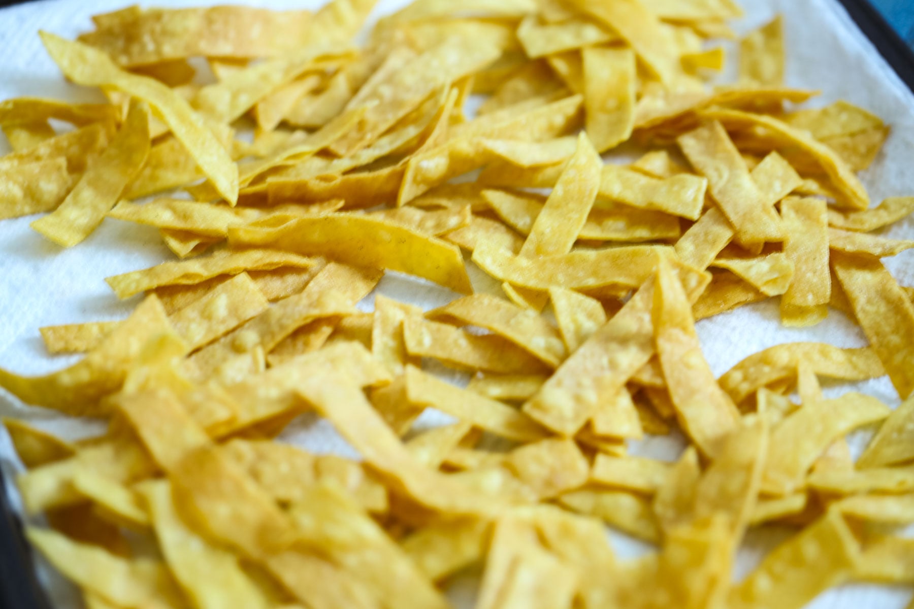 fried tortilla strips resting on a paper towel lined baking sheet.