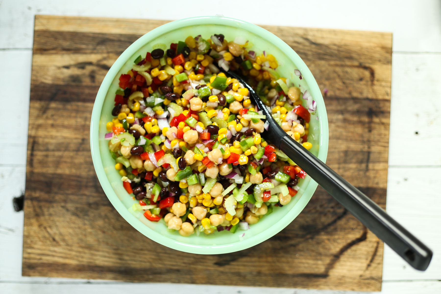 marinated bean salad in a green bowl with a serving spoon on a cutting board.