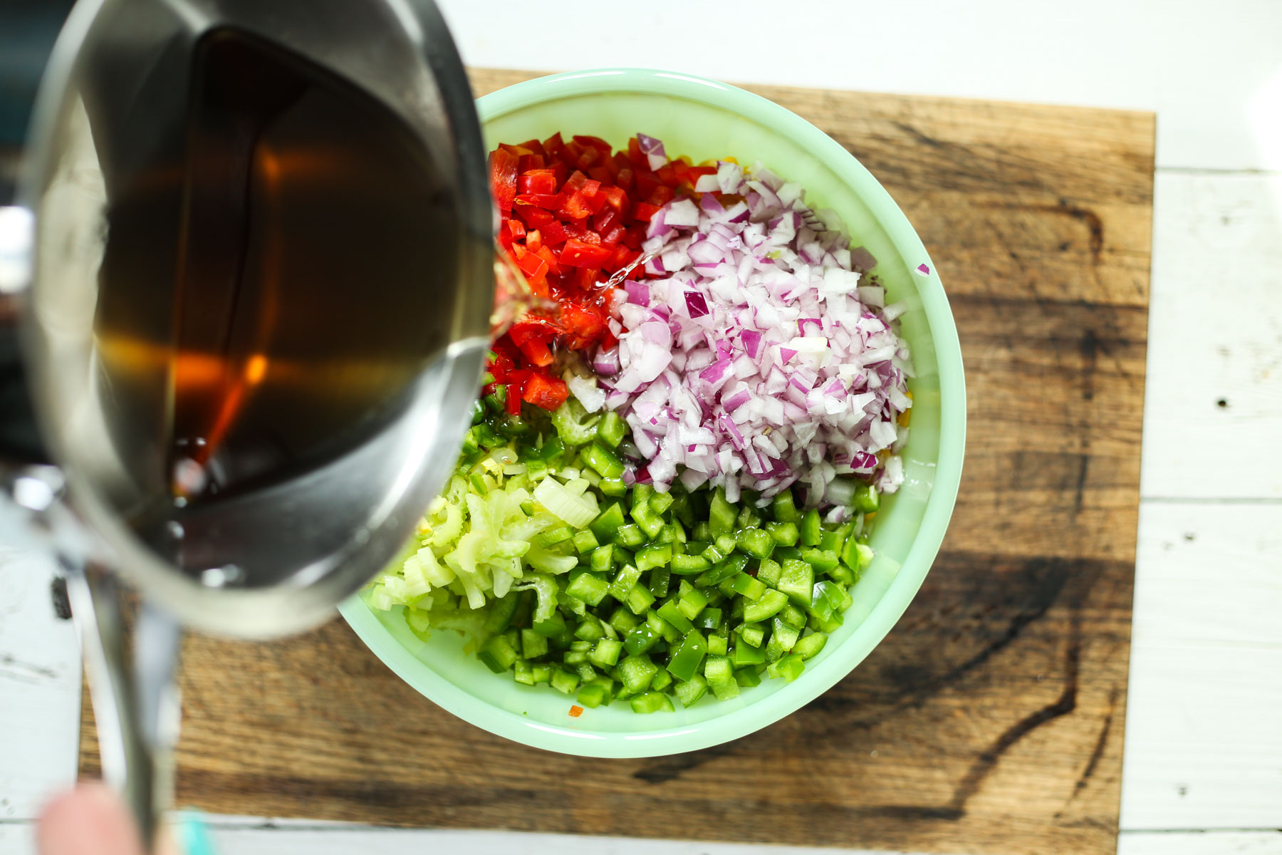 pouring dressing onto marinated bean salad in a green bowl on a cutting board.