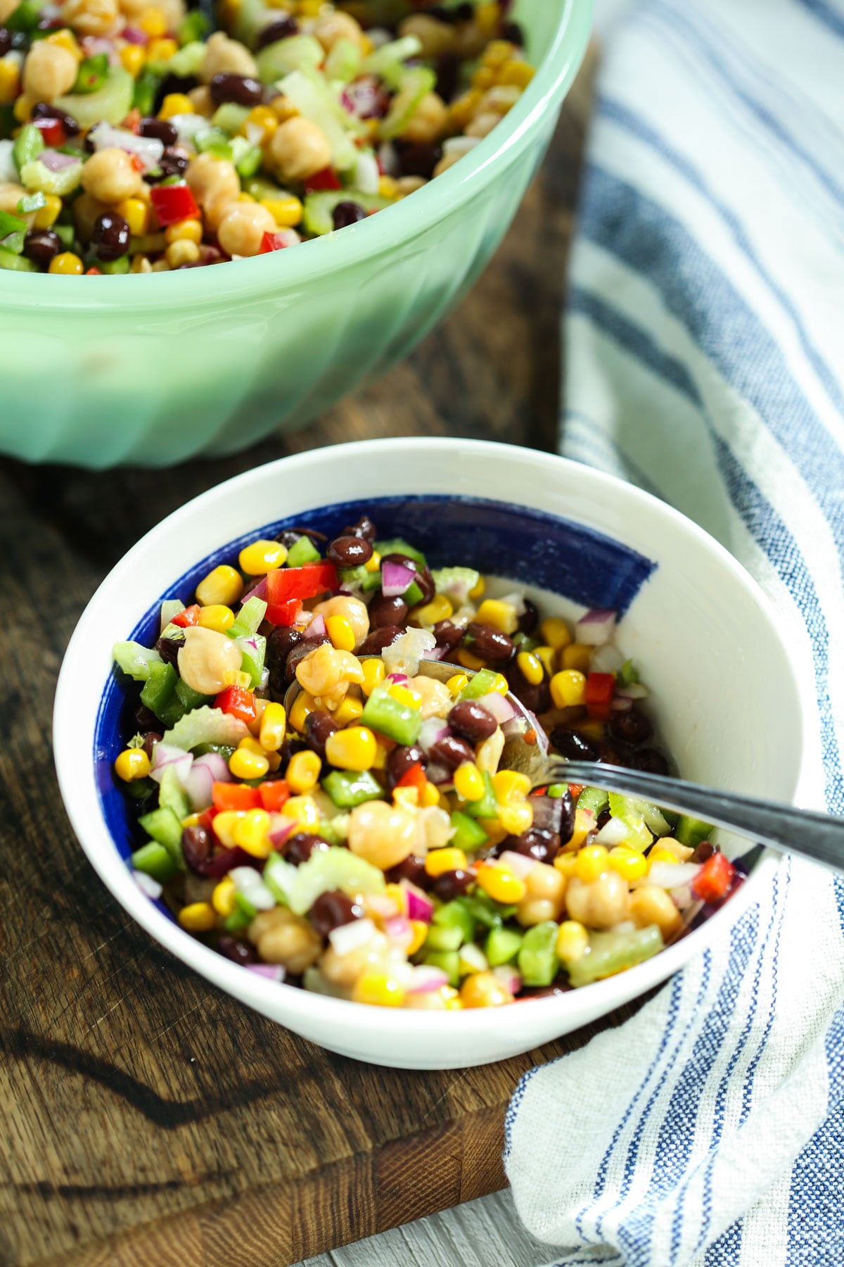 rainbow marinated bean salad in a white and blue bowl with a spoon and a striped napkin.