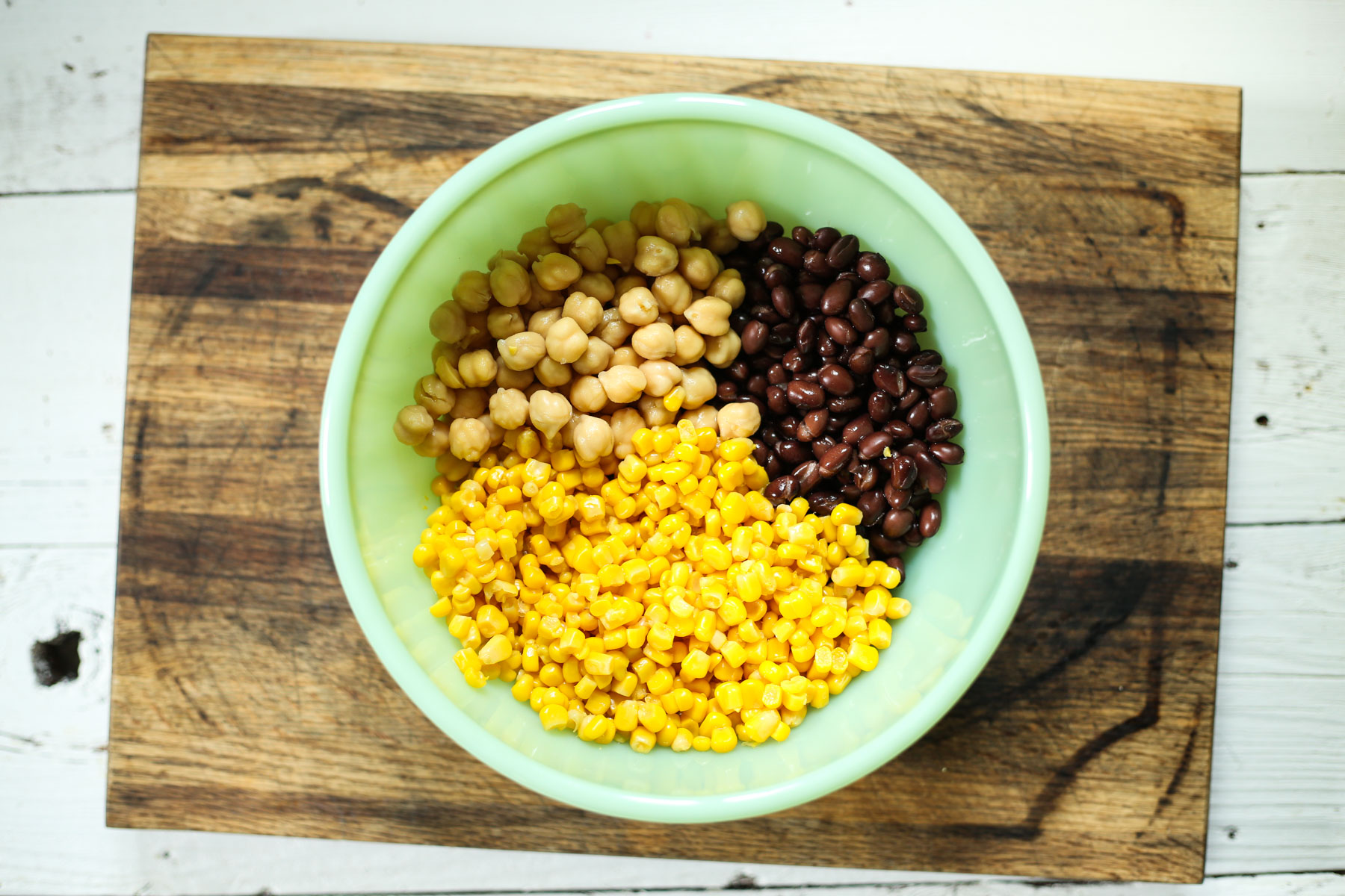 bean salad in a green bowl with a serving spoon on a cutting board.