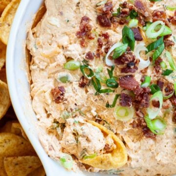 million dollar taco dip garnished with bacon bits and sliced green onion with a scoops corn chip being dipped into the dip.
