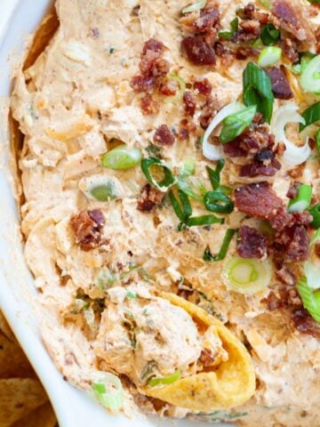 million dollar taco dip garnished with bacon bits and sliced green onion with a scoops corn chip being dipped into the dip.