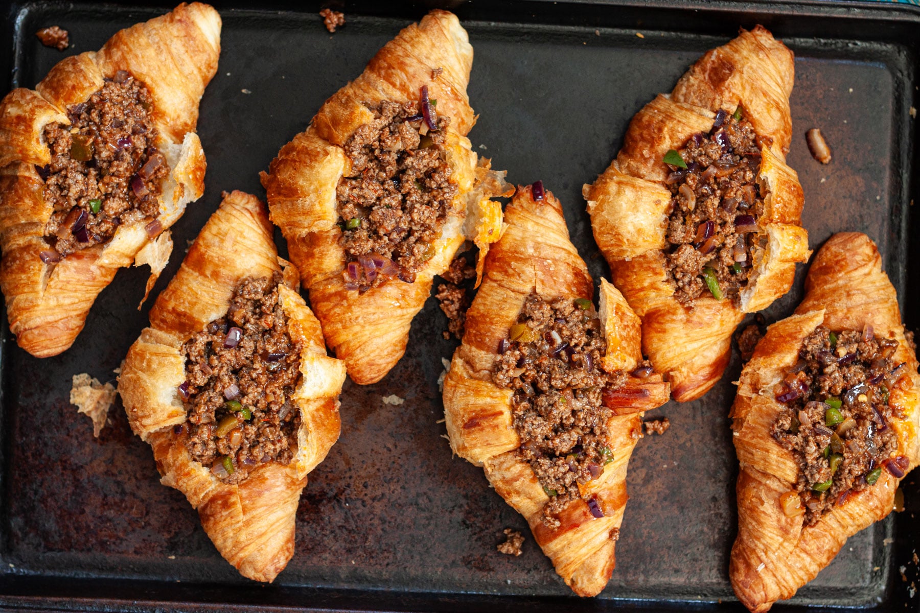 Six croissants on a baking sheet filled with taco seasoned ground beef.