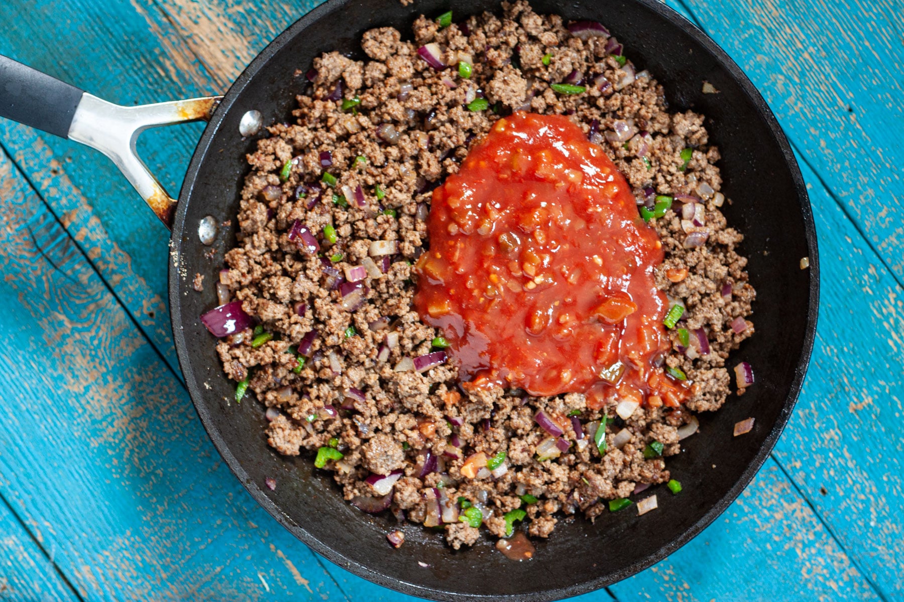 Salsa being added to the skillet of taco seasoned ground beef.
