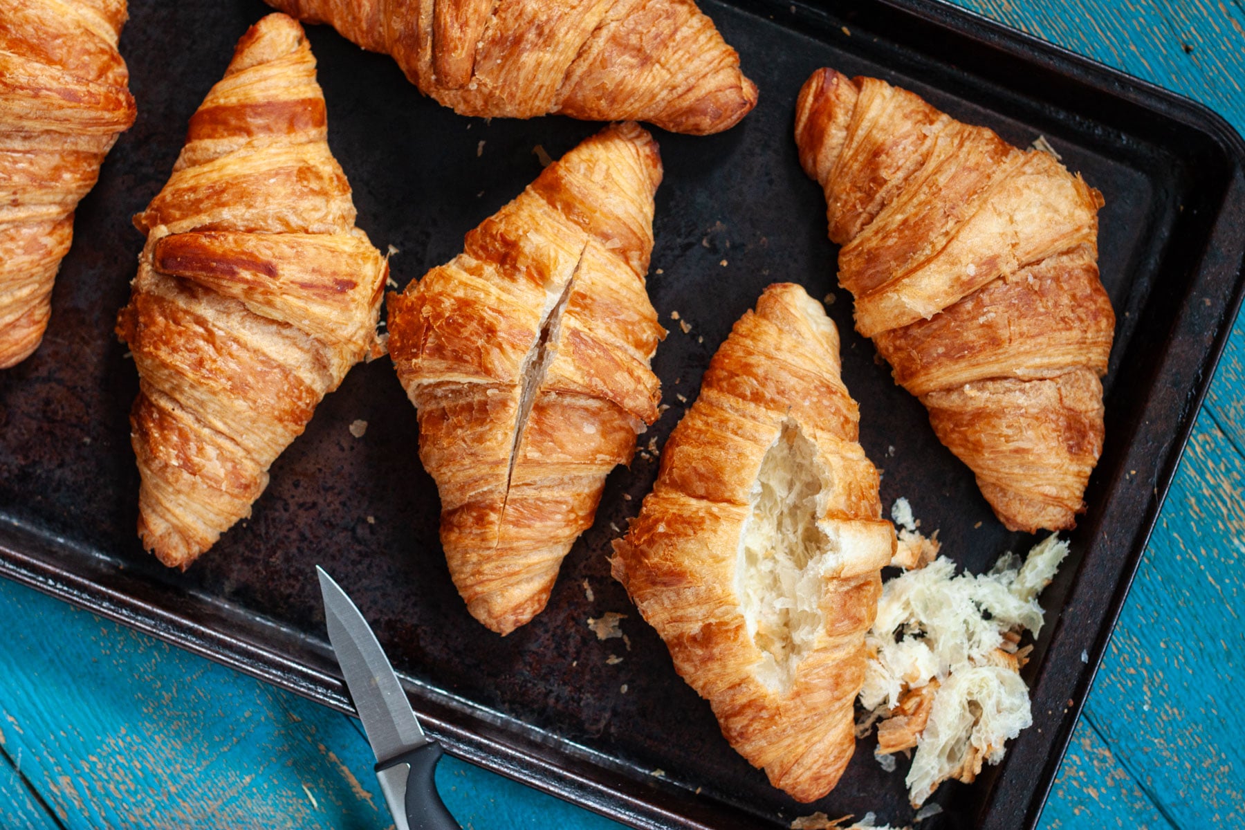 Croissants lined up on a baking sheet, with the center hollowed out of one of them. 