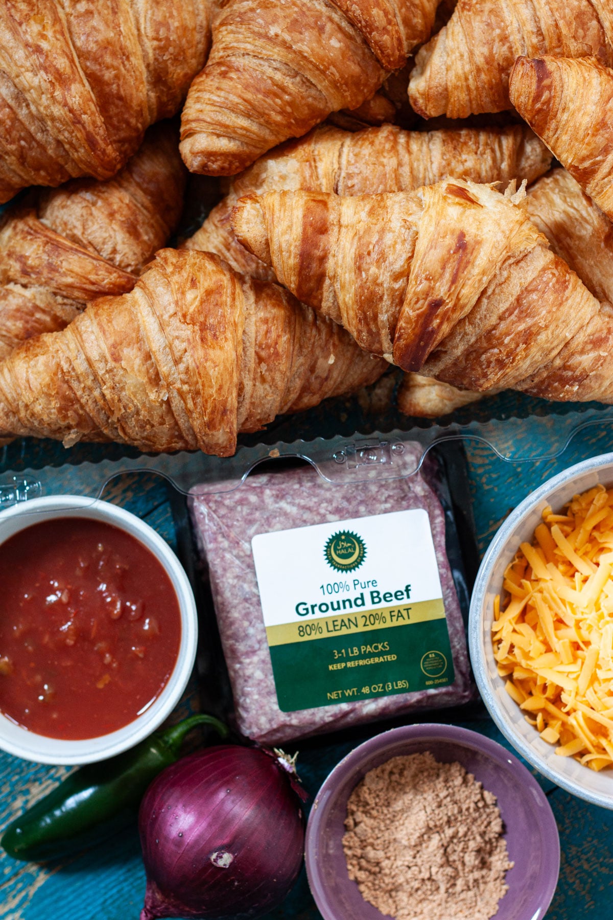 ingredients needed to make taco croissants including croissants, ground beef, taco seasoning, salsa, onion, and shredded cheese